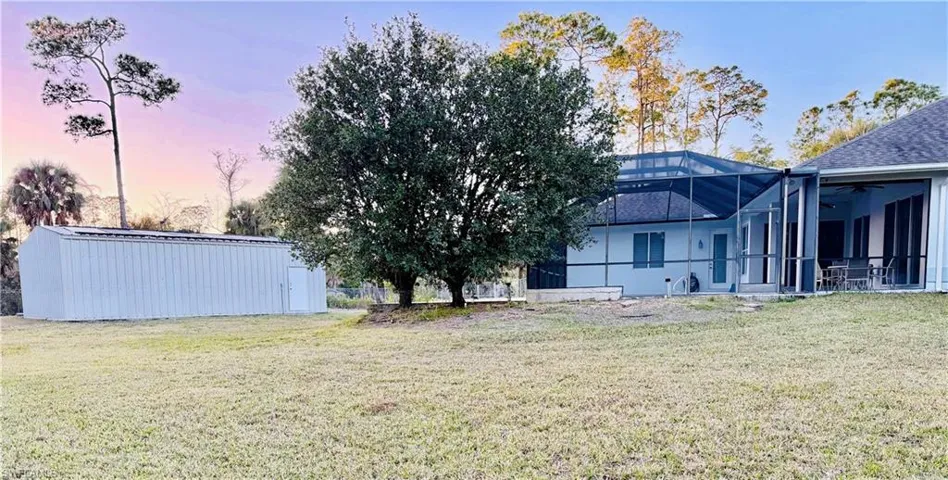 Rear view of house featuring glass enclosure, a lawn, an outdoor structure, a sunroom, and a patio