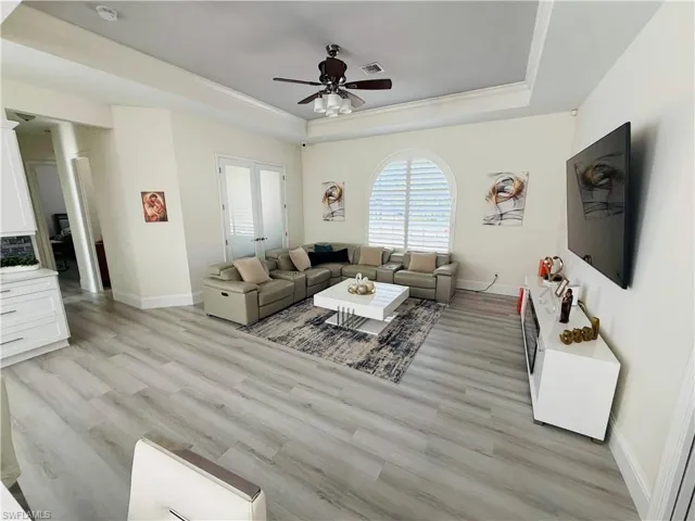 Living room with ceiling fan, light wood-style flooring, a tray ceiling, and ornamental molding