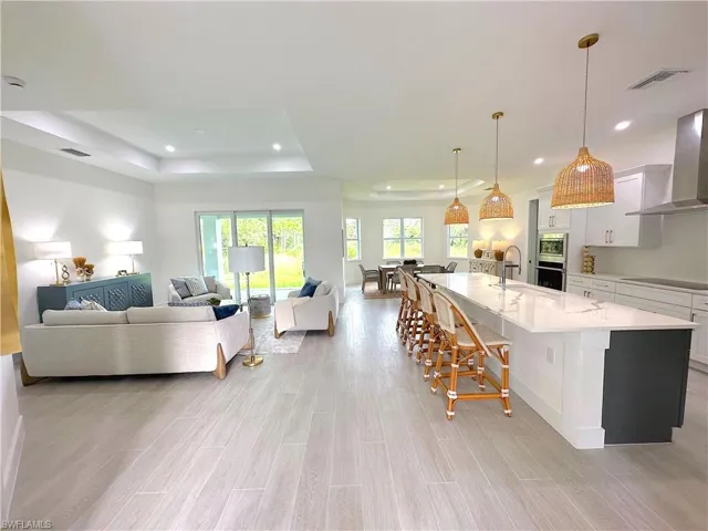 Kitchen featuring wall chimney range hood, a raised ceiling, a large island, pendant lighting, and white cabinets