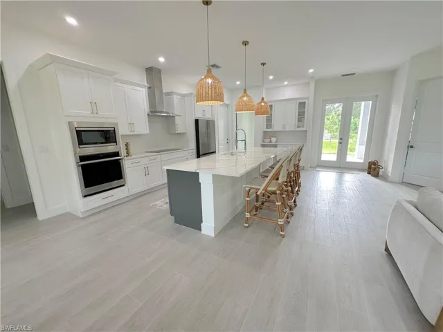 Kitchen with a spacious island, white cabinetry, wall chimney range hood, and stainless steel appliances