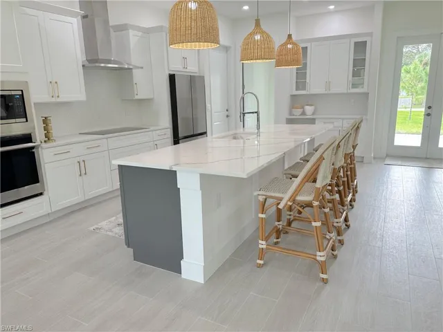 Kitchen featuring wall chimney range hood, sink, white cabinetry, stainless steel appliances, and a kitchen island with sink