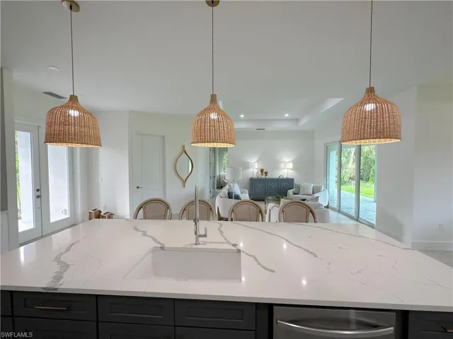 Kitchen with light stone countertops, sink, hanging light fixtures, and a wealth of natural light