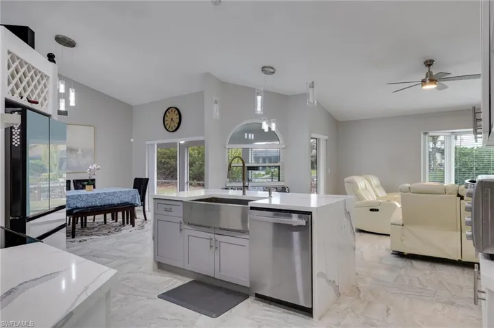 Kitchen featuring vaulted ceiling, open floor plan, dishwasher, a kitchen island with sink, and light stone counters