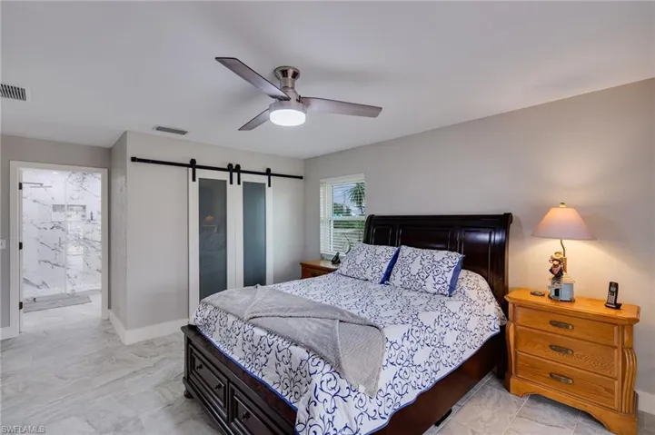 Bedroom with a barn door, ensuite bath, and ceiling fan