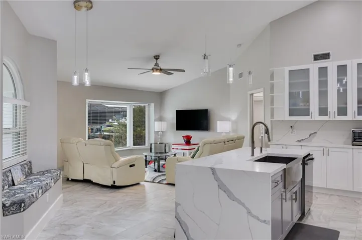 Kitchen with lofted ceiling, light stone countertops, white cabinetry, glass fronted cabinets, and open floor plan