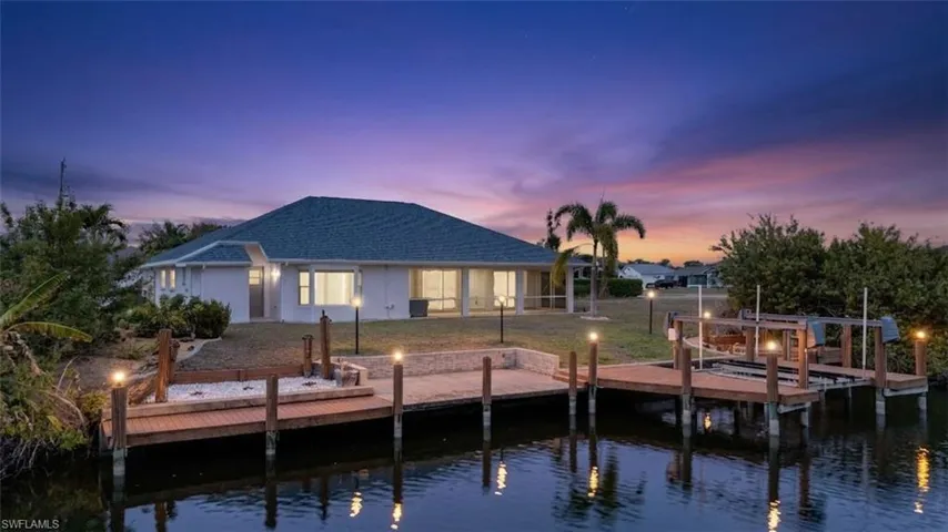 Back of property at dusk with a water view, boat lift, and a shingled roof