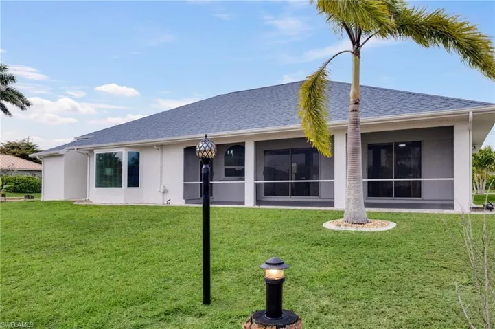 Back of property with a sunroom, a shingled roof, stucco siding, and a lawn