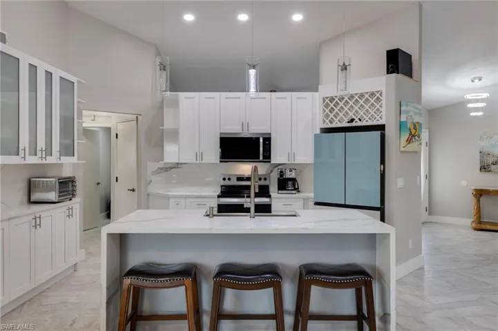 Kitchen featuring light stone counters, white cabinetry, pendant lighting, stainless steel appliances, and a high ceiling