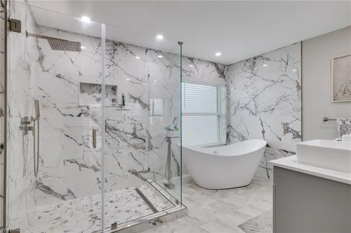 Bathroom featuring vanity, stone wall, a marble finish shower, recessed lighting, and a soaking tub