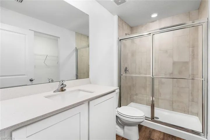 Bathroom featuring a textured ceiling, an enclosed shower, wood-type flooring, vanity, and toilet