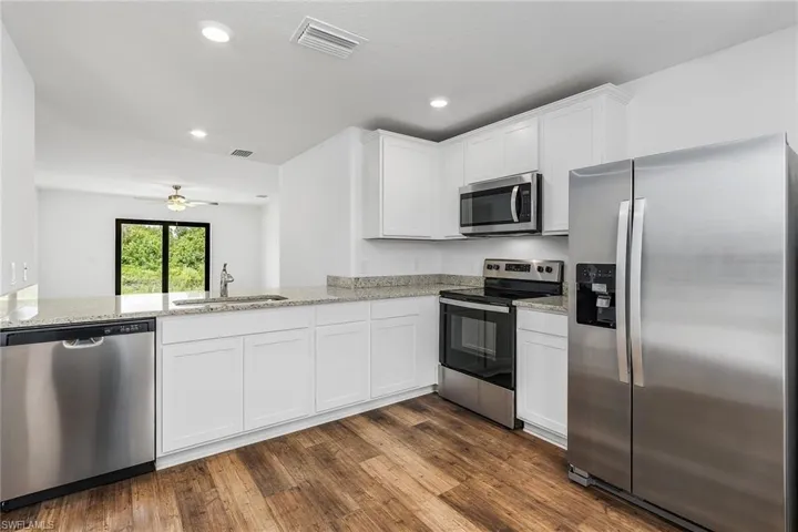 Kitchen with appliances with stainless steel finishes, white cabinets, sink, and dark hardwood / wood-style floors