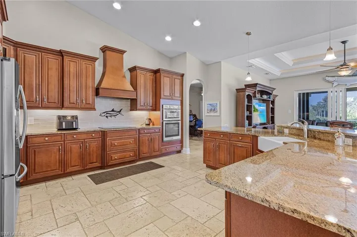 Kitchen featuring granite countertops, farm sink, stainless steel appliances, and custom range hood