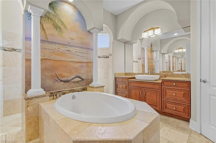 Bathroom featuring vanity, a relaxing tiled tub, and ornate columns