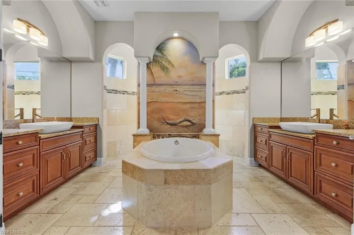 Primary Bathroom featuring decorative columns, dual vanities, a relaxing tiled tub, and tiled walk-through shower