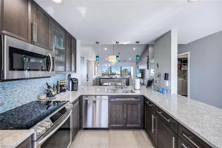 Kitchen with washer and clothes dryer, appliances with stainless steel finishes, decorative light fixtures, sink, and kitchen peninsula