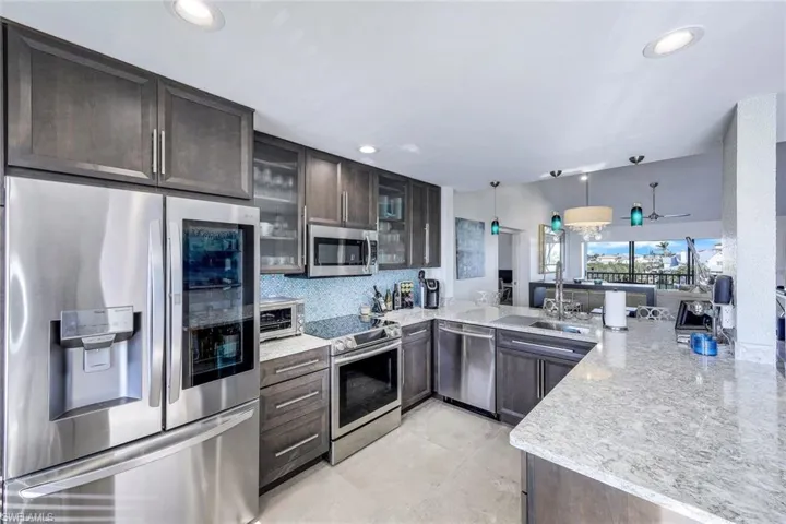 Kitchen featuring kitchen peninsula, appliances with stainless steel finishes, decorative light fixtures, light stone counters, and sink