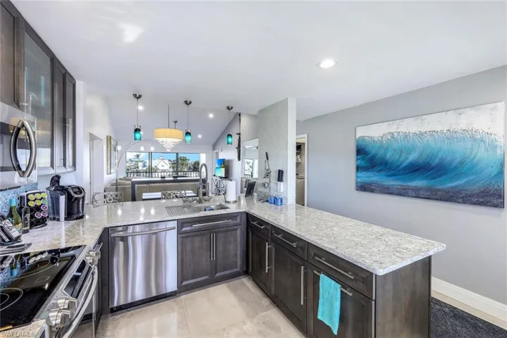 Kitchen featuring decorative light fixtures, kitchen peninsula, sink, light stone countertops, and stainless steel appliances