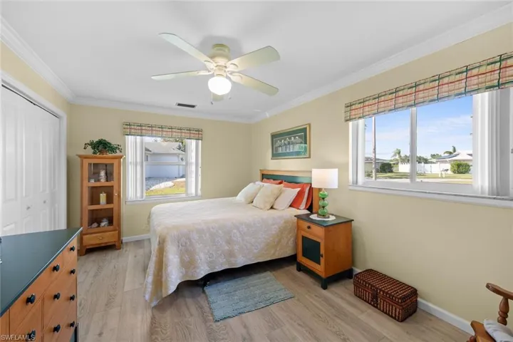 Bedroom featuring crown molding, ceiling fan, light wood-type flooring, multiple windows, and a closet