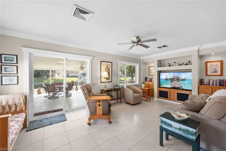 Living room featuring built in shelves, ceiling fan, light tile patterned flooring, and ornamental molding