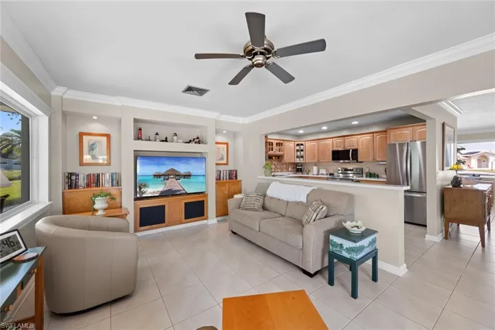 Living room featuring built in shelves, light tile patterned floors, and crown molding