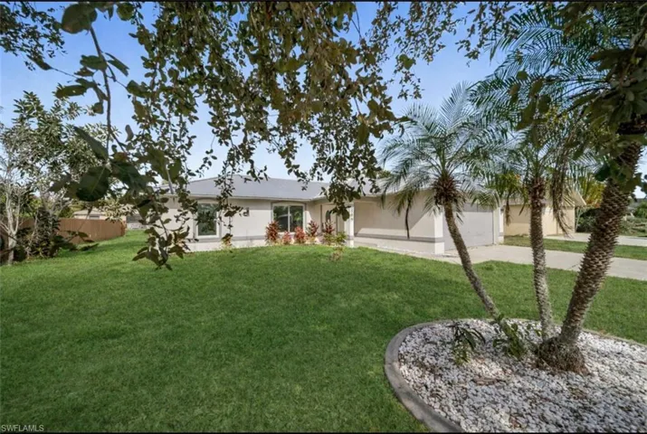 Rear view of property featuring concrete driveway, a yard, a garage, and stucco siding