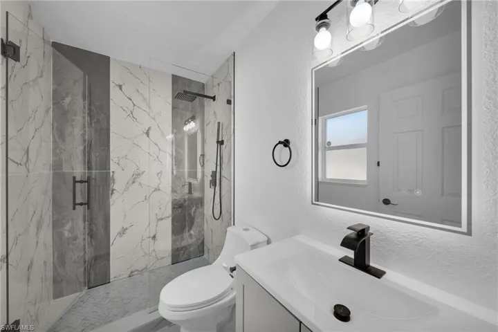 Bathroom featuring a marble finish shower, vanity, and a textured wall