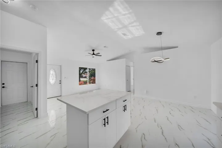 Kitchen with white cabinetry, hanging light fixtures, light stone counters, light marble finish flooring, and vaulted ceiling