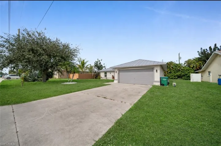 Ranch-style home featuring a front yard, driveway, a metal roof, a standing seam roof, and stucco siding