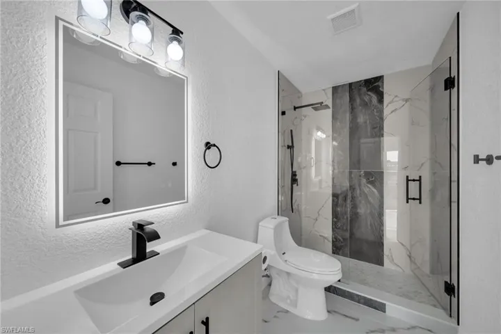 Bathroom with a textured wall, a marble finish shower, vanity, and marble tiled flooring
