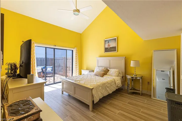 Bedroom featuring access to outside, wood finish floors, high vaulted ceiling, and a ceiling fan