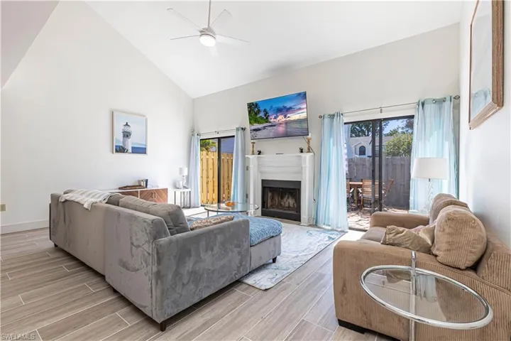 Living area with high vaulted ceiling, a fireplace, wood finish floors, and a ceiling fan