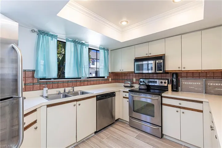 Kitchen featuring a tray ceiling, stainless steel appliances, crown molding, light countertops, and wood finish floors