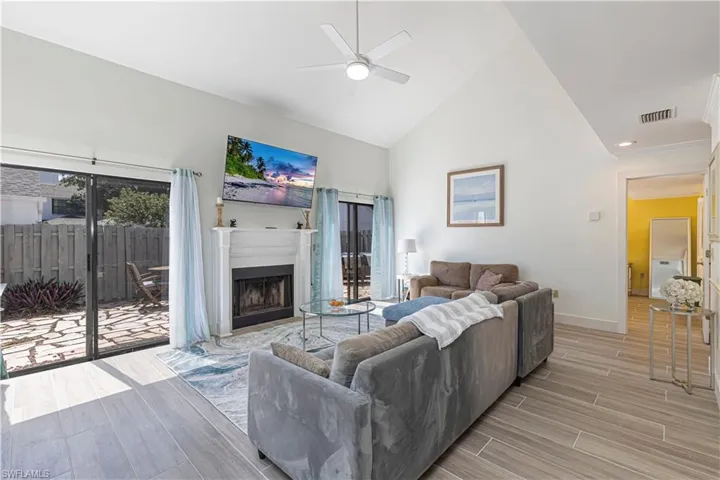 Living room featuring high vaulted ceiling, wood tiled floors, a fireplace with flush hearth, and ceiling fan