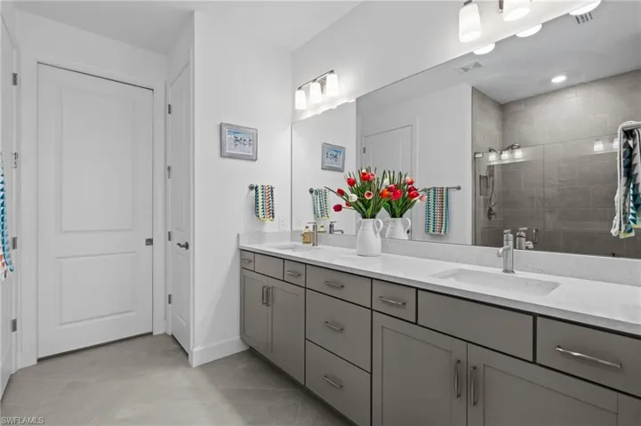 Full bathroom with tiled shower, double vanity, tile patterned flooring, and baseboards