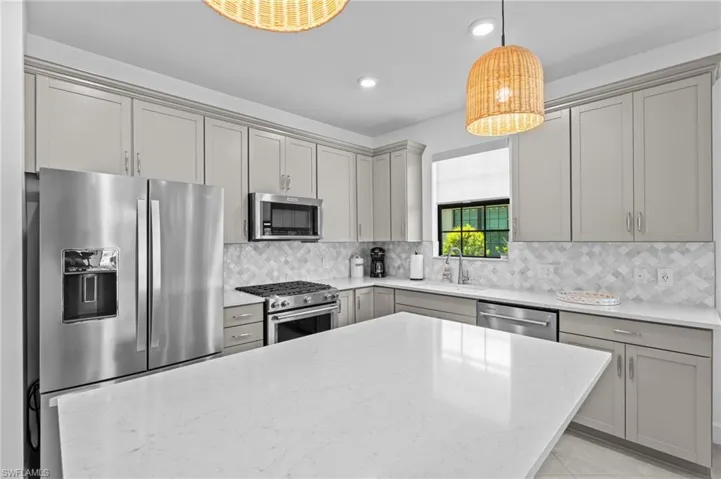 Kitchen featuring appliances with stainless steel finishes, gray cabinets, a sink, light stone countertops, and tasteful backsplash