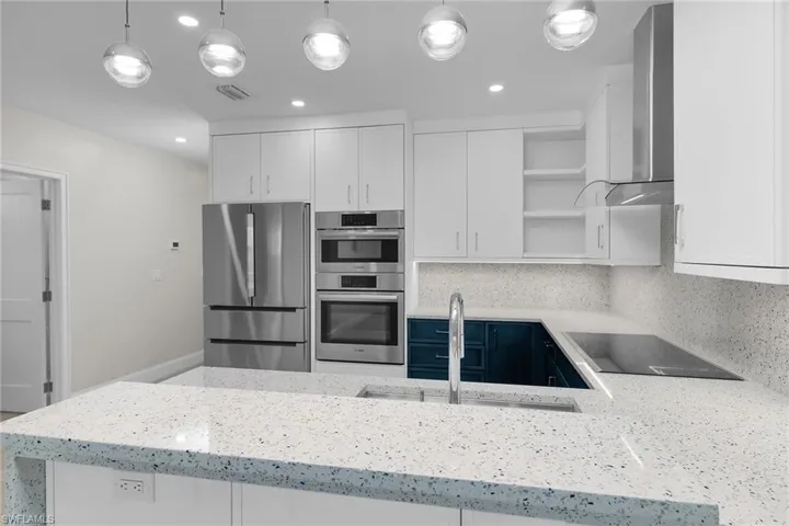 Kitchen featuring white cabinetry, open shelves, light stone counters, stainless steel appliances, and pendant lighting