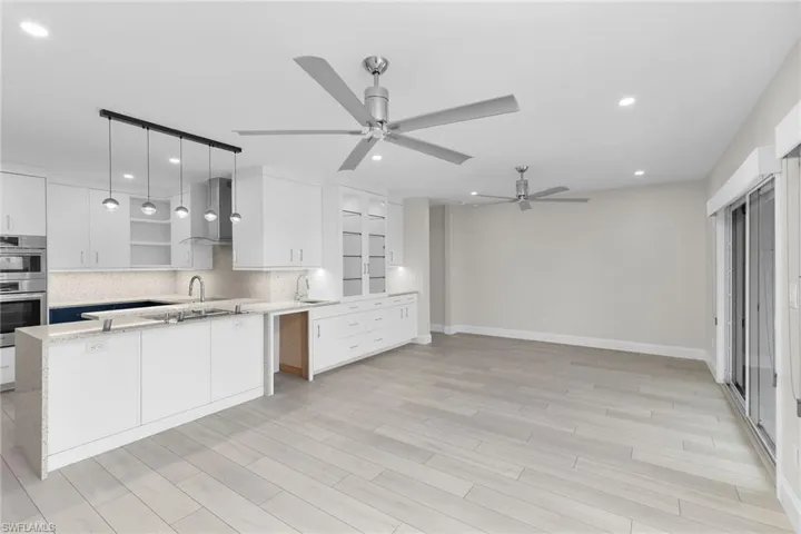Kitchen featuring white cabinets, light stone counters, decorative light fixtures, stainless steel double oven, and light wood-style floors