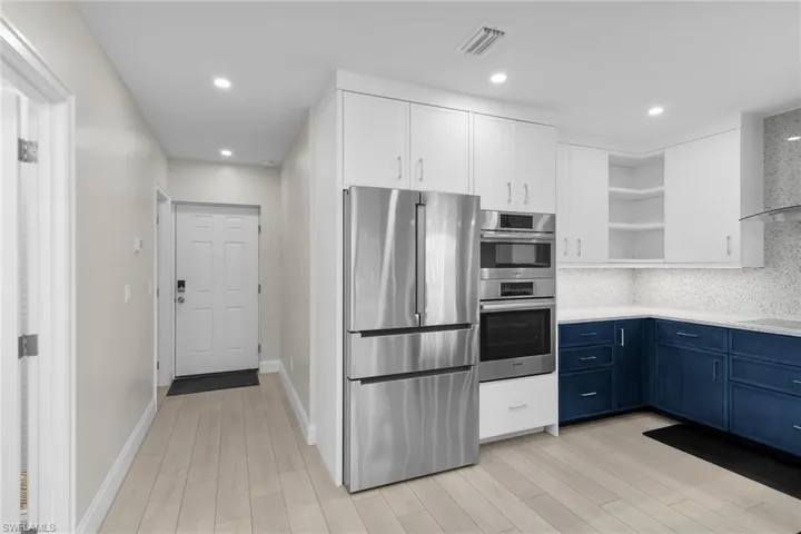 Two tone kitchen with two tone cabinets, stainless steel appliances, open shelves, decorative backsplash, and light wood-style floors