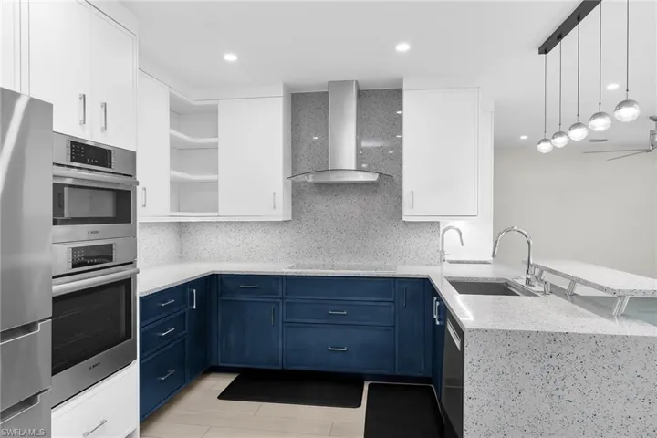 Dual tone kitchen with two tone cabinetry, light stone counters, open shelves, range hood, and hanging light fixtures
