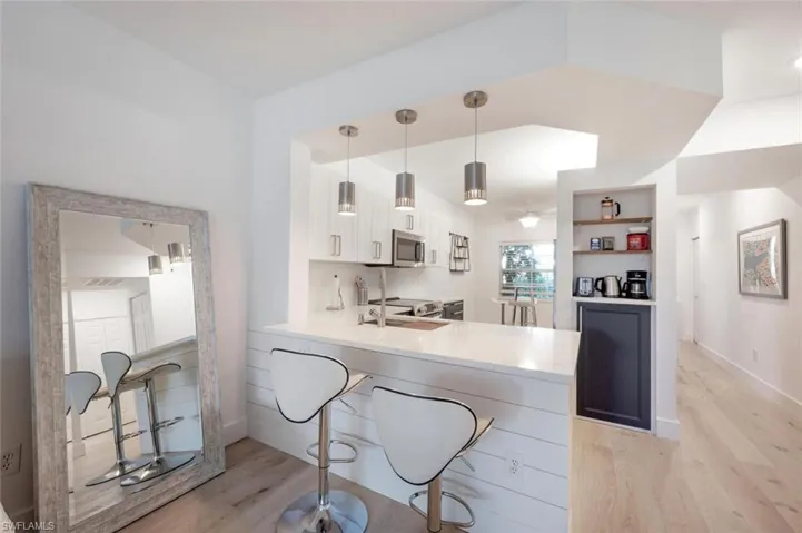 Kitchen featuring quartz counter top peninsula, white cabinets, hanging light fixtures, and light hardwood / wood-style floors