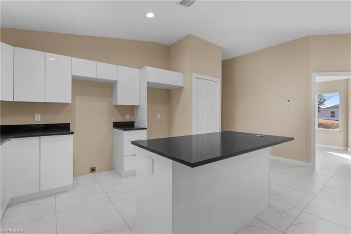 Kitchen with white cabinets, light marble finish floors, vaulted ceiling, a center island, and modern cabinets
