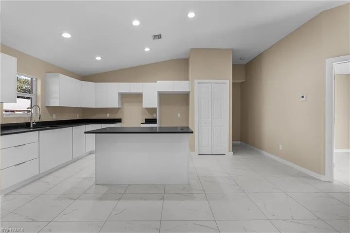 Kitchen with lofted ceiling, white cabinets, light marble finish floors, a kitchen island, and recessed lighting
