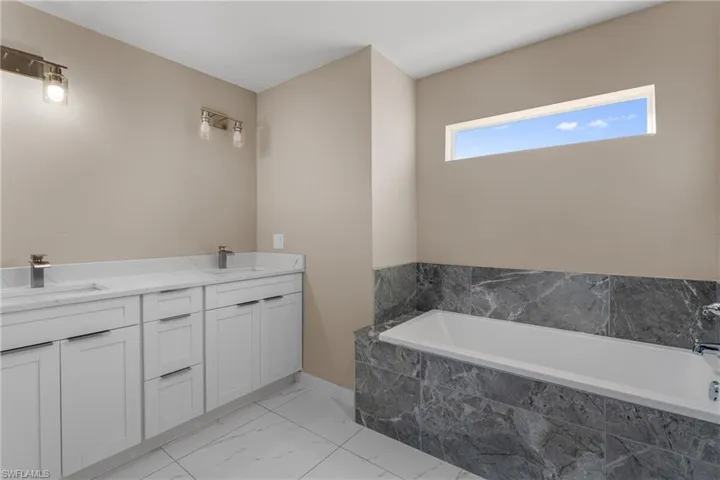 Bathroom featuring double vanity, light marble finish flooring, and a garden tub