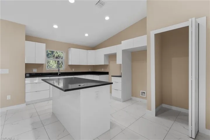 Kitchen with white cabinetry, recessed lighting, a center island, lofted ceiling, and light marble finish flooring
