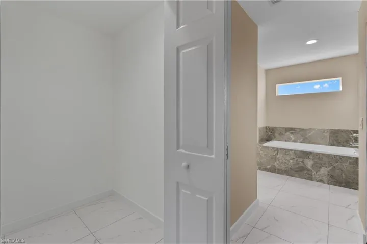 Full bath with light marble finish floors and a garden tub