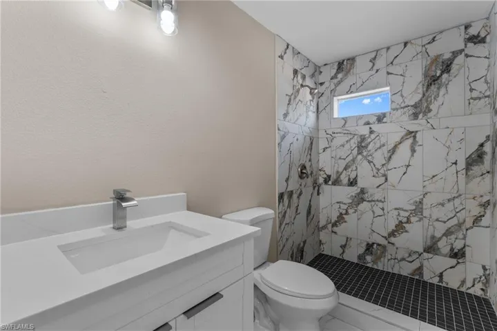 Bathroom featuring vanity, a marble finish shower, a textured wall, and marble look tile flooring