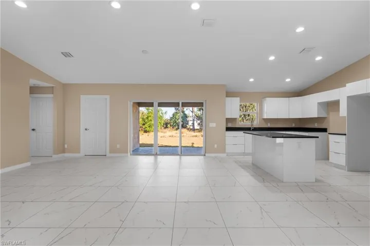 Kitchen featuring recessed lighting, white cabinets, vaulted ceiling, light marble finish floors, and open floor plan