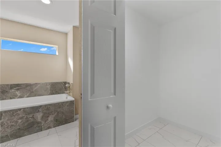 Bathroom featuring light marble finish flooring and a garden tub