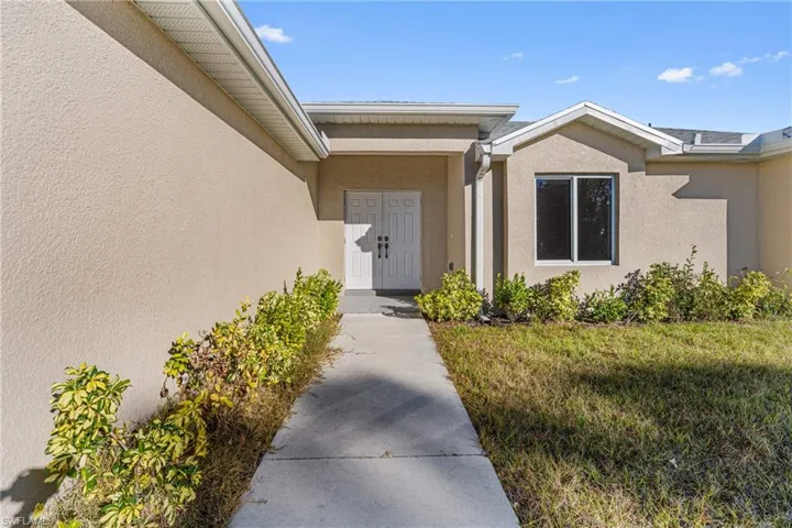 View of exterior entry with stucco siding and a yard