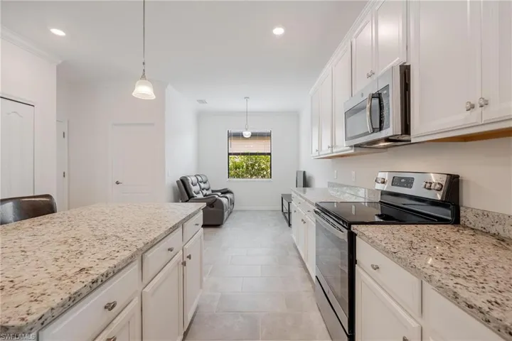Kitchen featuring ornamental molding, stainless steel appliances, white cabinets, pendant lighting, and light tile floors